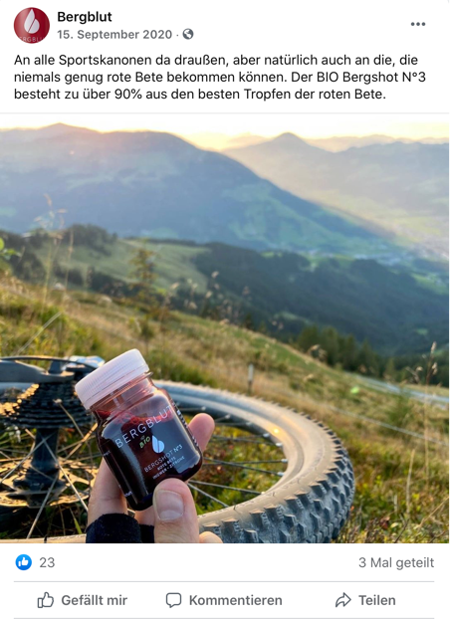 Grüne Wiesen und der Reifen eines liegenden Fahrrades sind im Bild zu sehen. Davor ist eine Hand mit einem blutroten Getränk von Bergblut zu erkennen. Dient als Beispiel für Nachhaltiges Marketing von der Blogseite Online Nachhaltig.