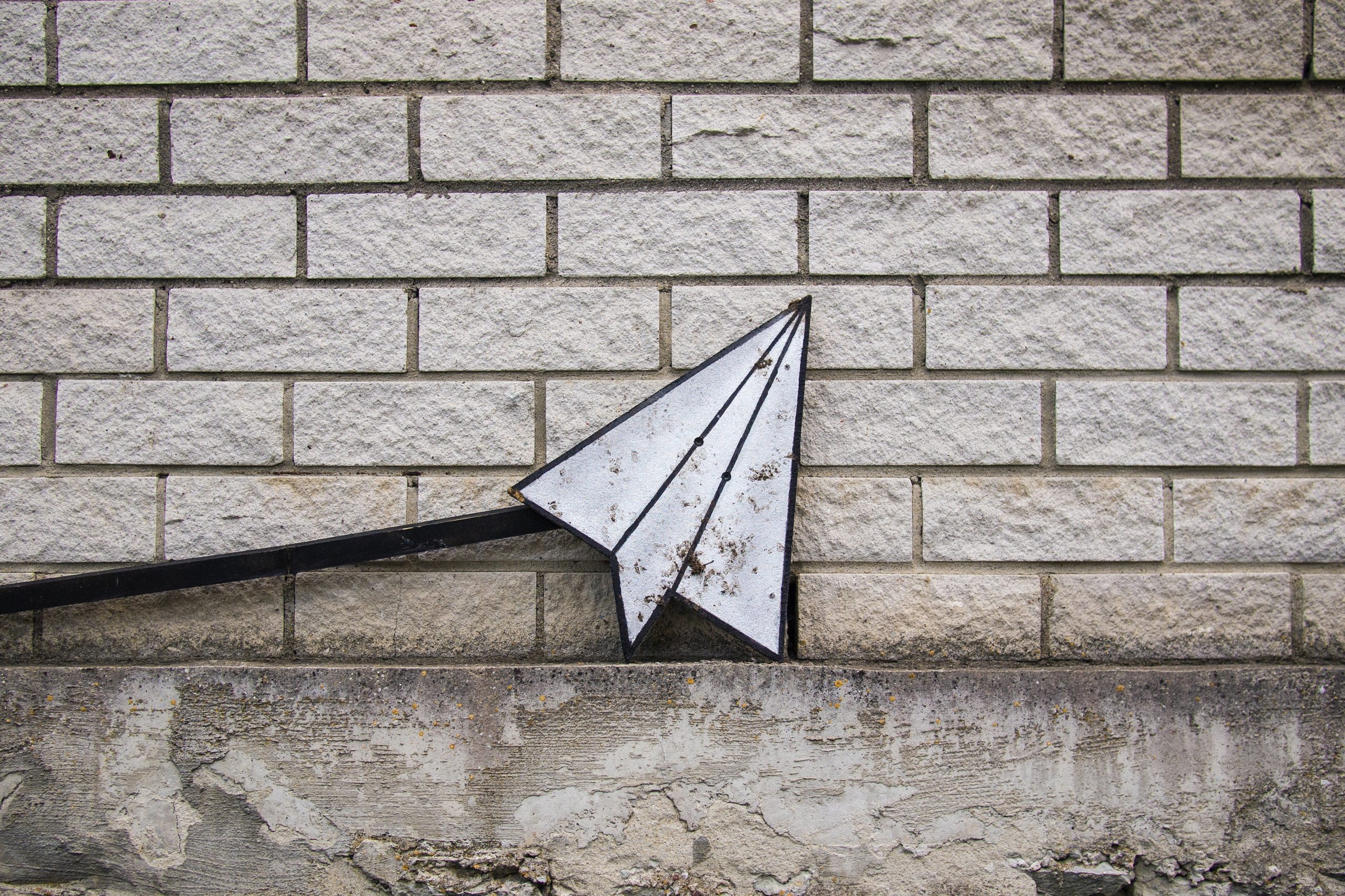 Grafik eines gefalteten Papierfliegers vor einer hellen Ziegelwand